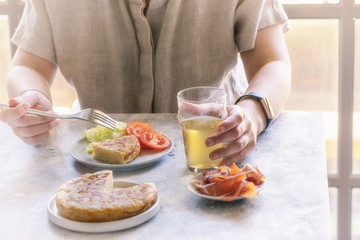 Person eating Spanish Tortilla,  served with traditional slices of jamon, Iberian ham,  beer and salad on the local restaurant. Lifestyle image.