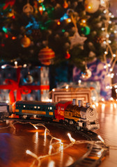 toy vintage steam locomotive on the floor under a decorated Christmas tree on a background of bokeh lights garland.