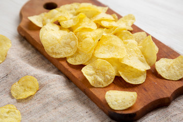 Yellow potato chips with salt on a rustic wooden board, side view. Close-up.