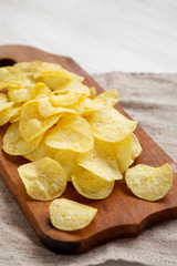 Tasty potato chips with salt on a rustic wooden board, side view. Closeup.