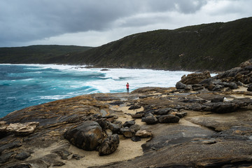 Girl standing at the edge of a cliff watching the rough waves crash against the cliff. Moody sky...
