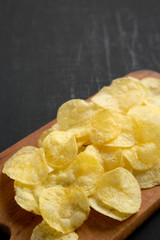 Crispy potato chips with salt on a rustic wooden board on a black background, side view. Copy space.