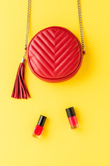 Overhead shot of red woman’s purse with nail polishes on yellow background. Flat lay