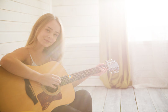 Attractive woman with guitar sitting in light room with wooden floor. Musician, concert, hobby, leisure, rehearsal concept