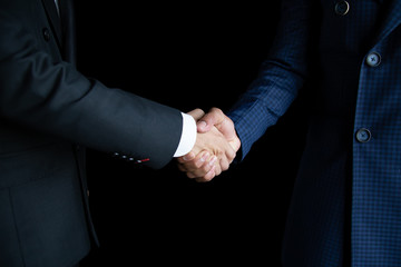 Obraz premium The business man in a black suit and a blue suit holding hands to make business deals on a black background.