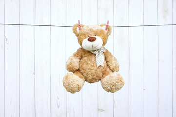 Bear dried on a rope after washing on a light wooden background. Toy bear hanging by the ears on clothespins.