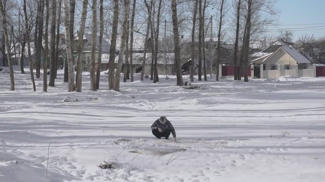 Man beats on domestic carpet on the snow in winter to clean and vacuuming rug. Strange Russian tradition or custom. One shakes out rug to remove dust and dirt