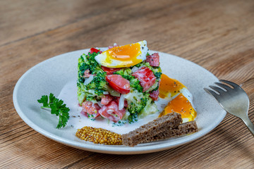 Delicious salad with broccoli, tomato, onion and boiled egg with cream sauce in plate on wooden background. Healthy food