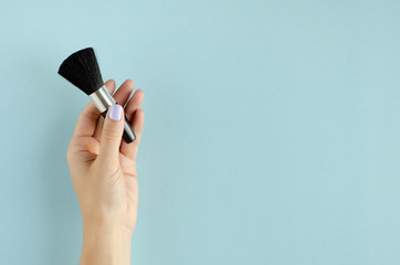 Hand with makeup brush composition on blue background.