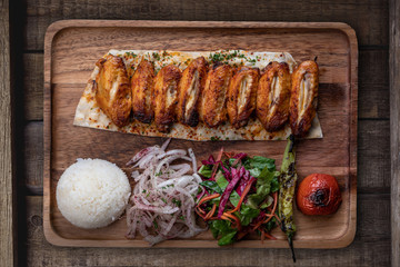 Turkish chicken wings kebab with rice and vegetables isolated on rustic wooden table
