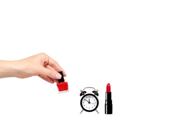 Hand with red nail polish, lipstock and alarm clock.