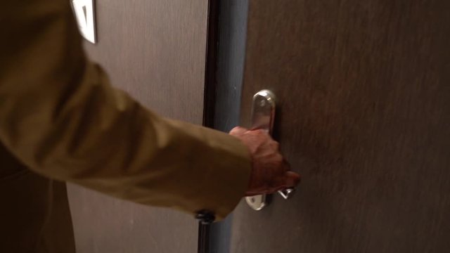 A slow motion view showing hands of a man in brown blazer opening the door of a room to enter/exit.
