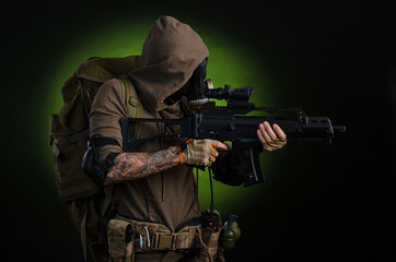 man Stalker with a gun with a telescopic sight and a backpack in a gas mask on a dark background with emotions looking, aiming, watching, sneaking