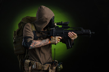 Fototapeta premium man Stalker with a gun with a telescopic sight and a backpack in a gas mask on a dark background with emotions looking, aiming, watching, sneaking