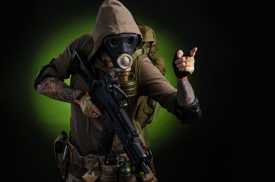 man Stalker with a gun with a telescopic sight and a backpack in a gas mask on a dark background with emotions looking, aiming, watching, sneaking