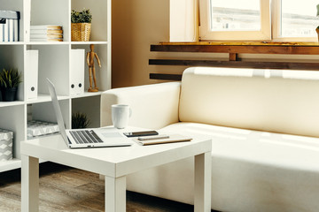 Open laptop on table near sofa, home interior. Freelancer workplace concept