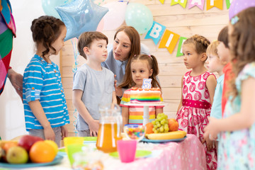 Fototapeta premium Group of adorable kids, birtday boy and his mom gathered around festive table. Birthday party for preschoolers