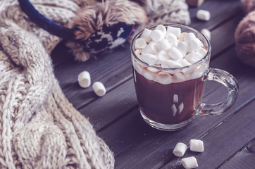 Hot cocoa with marshmallows in a glass cup surrounded by Christmas gifts and winter clothes, Christmas atmosphere and coziness