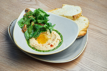 Traditional chickpea hummus in bowl with salad, bread, eggplant and mushrooms. Israeli cuisine. Snack. Wooden background
