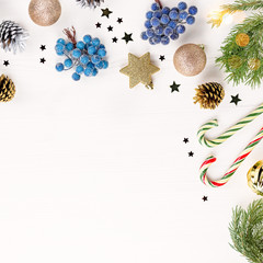 Blue christmas ornaments and golden decorations on white table with candy cones and pine tree flat lay, copy space. Christmas border in blue, green and gold colors
