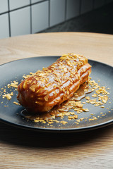 Appetizing and large eclair with glaze of salted caramel on top and fir cream inside on a black...