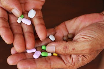 Closeup at elderly Asian man hand is holding many pills(tablet and capsule) in hands taking a lot of medicine, supplements or antibiotic antidepressant painkiller medication Hope for cure.