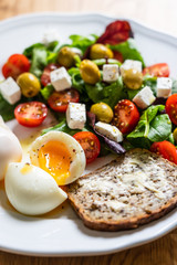 Greek salad with sandwich and boiled egg on white plate