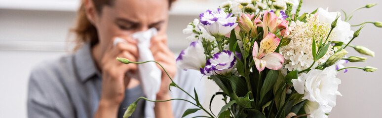 Fototapeta na wymiar panoramic shot of bouquet of flowers near woman with pollen allergy sneezing in tissue