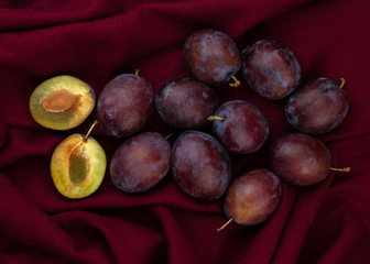 Fresh organic plums on burgundy background. Still life of ripe and juicy fruits