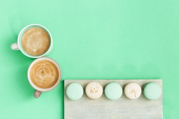 Cup coffee and tasty macaroons for breakfast on mint paper background. Cozy morning hot drinks and sweets for couple of people. Top view with copy space.
