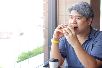 An elderly Asian man is eating hamburgers in a restaurant.