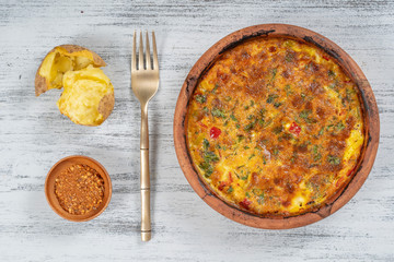 Ceramic bowl with vegetable frittata, simple vegetarian food. Frittata with tomato, pepper, onion and cheese on wooden table, close up. Italian egg omelette