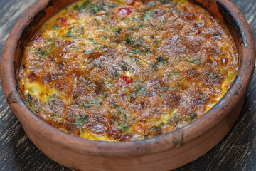Ceramic bowl with vegetable frittata, simple vegetarian food. Frittata with tomato, pepper, onion and cheese on wooden table, close up. Italian egg omelette