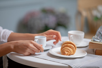 Side view of female hands holding cup of coffee. Woman having coffee brake in French cafe. Women drinking coffee in French styled restaurant. Croissants and coffee on white table.