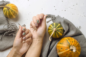 Trend manicure in autumn colors on a gray table next to pumpkins and a gray scarf