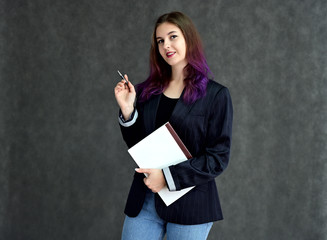 Studio portrait of a pretty brunette student girl with long hair in a jacket on a gray background. Smiling at camera with emotions in various poses.