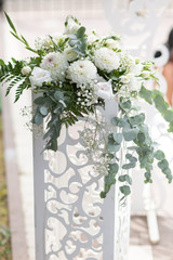 Wedding white wooden arch decorated with flowers outdoors. Beautiful wedding set up. Wedding ceremony on green lawn in the garden. Part of the festive decor, floral arrangement. Vertical photo.