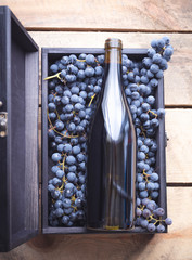 Bottle of freshly made wine with box of grapes on wooden background