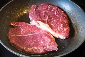 roasting two beefsteaks in frying pan on range