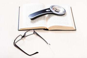 eyeglasses and magnifier on open book on table