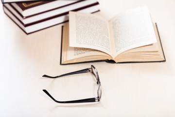 spectacles and open book near stack of books