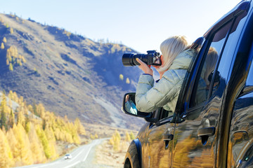 Happy tourist travelling in countryside. Tourist woman in an open window of a auto car taking...
