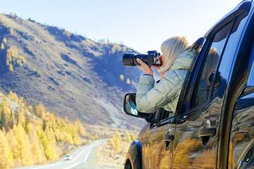 Happy tourist travelling in countryside. Tourist woman in an open window of a auto car taking photography. Blogger using hobby content concept, enjoy trip.