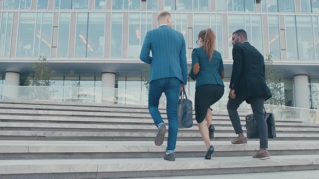 Confident team members walking on stairs in slow motion. Business men and woman in formal suits go and talk on the background of modern office building