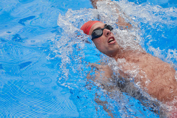 swimmer in an outdoor pool, swimming on his back, left arm raised and right down