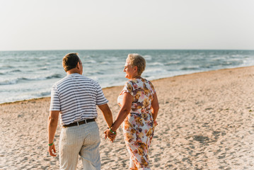 Romantic adult couple standing together on the beach. Mature pair relax at the seaside on holiday. Happy familiy walking and holding hands near sea. Husband embracing wife. Love story near the sea
