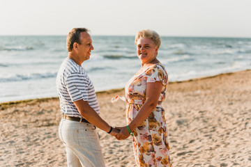 Romantic adult couple standing together on the beach. Mature pair relax at the seaside on holiday. Happy familiy walking and holding hands near sea. Husband embracing wife. Love story near the sea