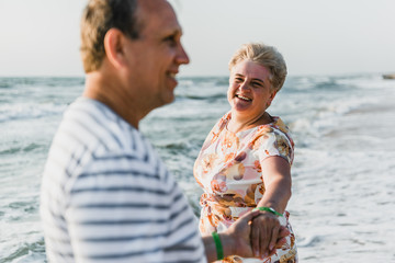 Romantic adult couple standing together on the beach. Mature pair relax at the seaside on holiday. Happy familiy walking and holding hands near sea. Husband embracing wife. Love story near the sea