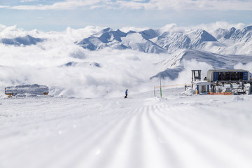 Fototapeta na wymiar Snow velvet on ski slope on the background of snowy mountain peaks. Prepared ski and snowboard track with trace of snow groomer on snow.