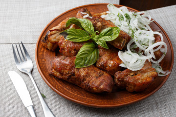 Grilled pork ribs in brown clay bowl close-up. Front view of plate with grilled pork ribs with onion and basil. Grey background. horizontal photo. Top view